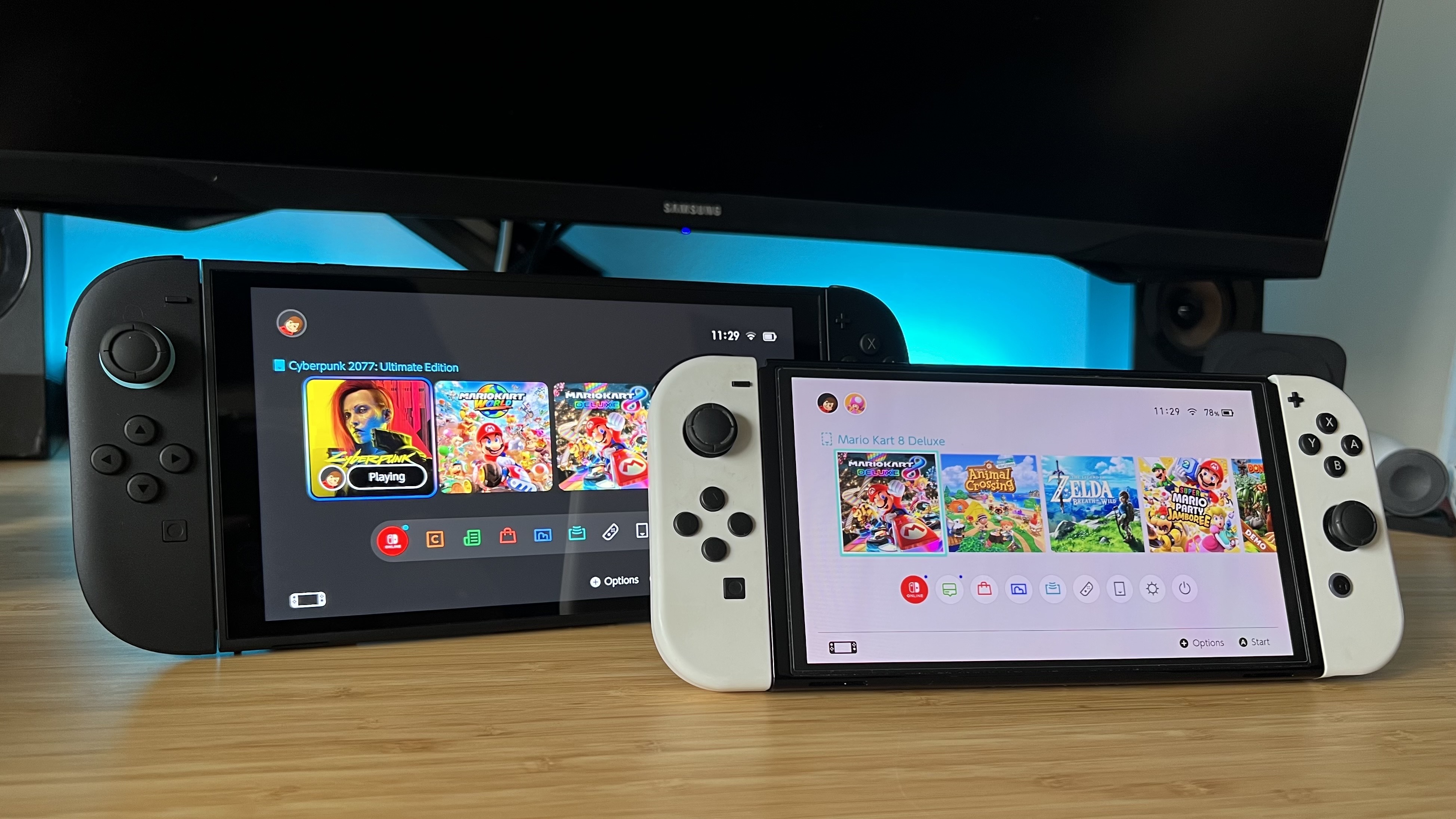 Nintendo Switch 2 and Nintendo Switch OLED on a wooden desk with blue backlighting