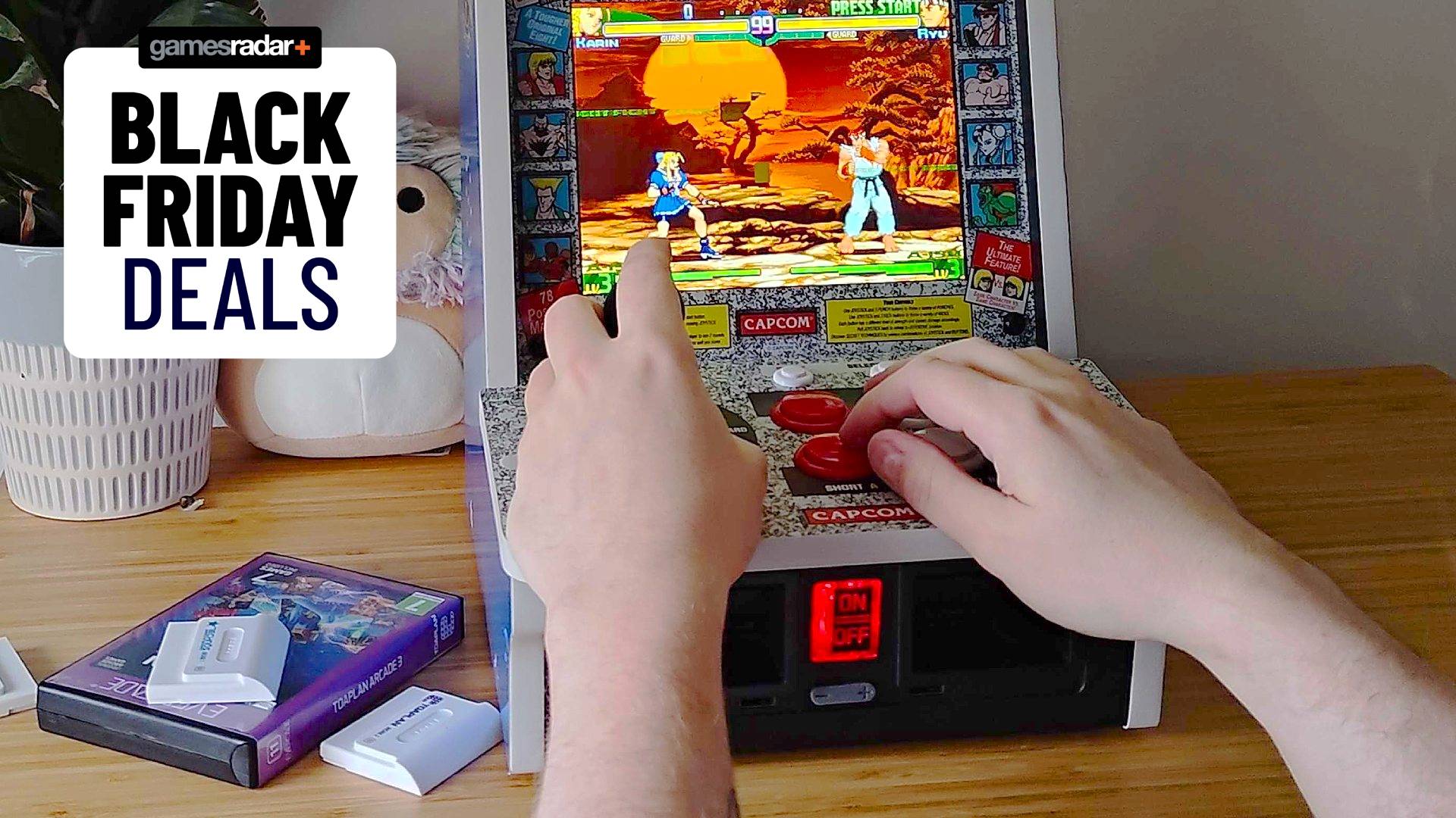 Black Friday deals GamesRadar+ badge at top left next to Evercade Alpha arcade machine with hands using controls to play Street Fighter Alpha.